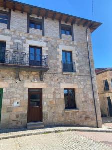 - un bâtiment en pierre avec une porte en bois et un balcon dans l'établissement Apartamentos Rurales La Plaza 2, à Duruelo de la Sierra
