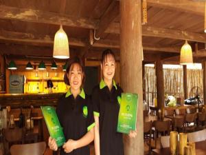 two women standing in a restaurant holding up green signs at Pu Luong Homestay & Tours in Hương Bá Thước
