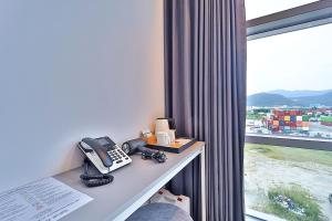 Zimmer mit einem Schreibtisch, einem Telefon und einem Fenster in der Unterkunft Browndot Signature Hotel in Yongjae