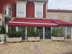 un restaurante con toldo rojo y plantas en ollas en hotel asador versus en Burgos