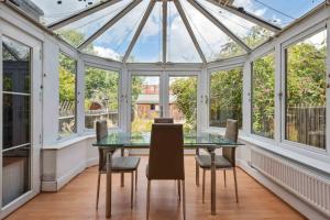 un salón acristalado con techo de cristal, mesa y sillas en Cozy Stay Rooms en Raynes Park