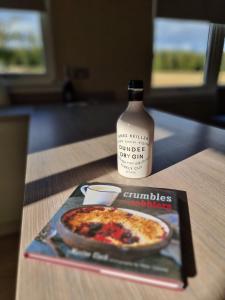 ein Buch und eine Pizza auf dem Tisch mit einer Flasche in der Unterkunft Muirton Cottage in Brechin