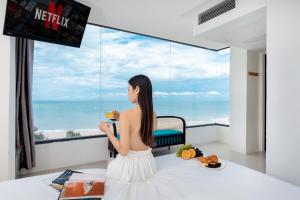 una mujer sentada en una mesa mirando por una ventana al océano en Annata Beach Hotel, en Vung Tau