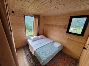 Cama pequeña en habitación de madera con 2 ventanas en Guest cottage - Nanka's house en Batumi