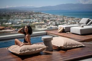 una mujer sentada en una almohada al borde de una piscina en Alectrona Living Crete, Olīvea Luxury Apartment en Plataniás