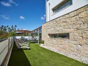 una pared de piedra con sillas y una sombrilla en el césped en Fonte Seca GuestHouse, en Leiria