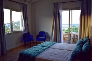 corail royal hotel في طبرقة: غرفة نوم بسرير وكرسيين ازرق ونوافذ