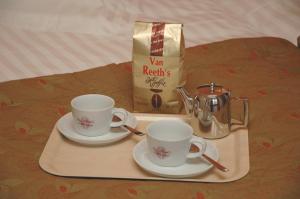 due tazze e piattini su un vassoio su un letto di Hotel Van Reeth's Koffiebranderij a Puurs