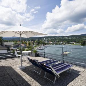 eine Terrasse mit einem Tisch, einem Sonnenschirm und einer Bank in der Unterkunft Hotel Garni Ogris Am See in Velden am Wörthersee