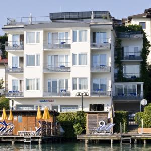 a building on the water with chairs and a dock at Hotel Garni Ogris Am See in Velden am Wörthersee