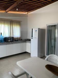 a white kitchen with a table and a refrigerator at Flat amplo em condominio beira mar in São Miguel do Gostoso