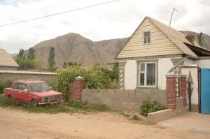 um velho carro vermelho estacionado em frente a uma casa em Guest House Aktilek em Tërt-Kul'