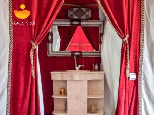 a bathroom with red curtains and a sink and a mirror at Arena y Sol Merzouga Camp in Merzouga