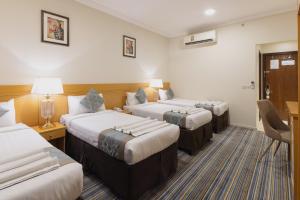 a hotel room with three beds and a desk at Snood Al Maaly Hotel in Makkah