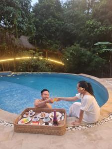 un homme et une femme assis dans une piscine dans l'établissement The Osing Bamboo Resort - a LIBERTA Collection, à Banyuwangi