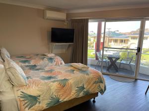 a bedroom with a bed and a balcony with a television at Ulladulla Harbour Motel in Ulladulla