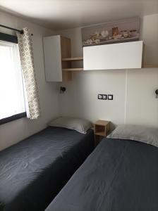 two beds in a small room with a window at Mobil home moderne neuf et ultra équipé de 6 à 8 couchages in Canet-en-Roussillon