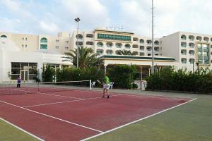 a man playing tennis on a tennis court in front of a building at appt Mahari in Yasmine
