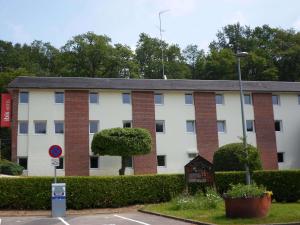 un edificio blanco y de ladrillo con un letrero en un aparcamiento en ibis les Etangs des Moines en Fourmies