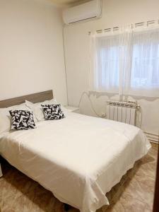 Un dormitorio con una cama blanca con almohadas y una ventana en Pensión el Carmen, en Alcobendas