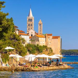 a group of people sitting on a dock with umbrellas on the water at Apartments Ivanovski in Rab
