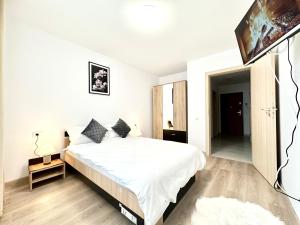 a white bedroom with a large bed and a flat screen tv at Urban Plaza Astra - Rise Private Apartments & Suites in Braşov