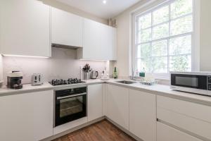 a white kitchen with white cabinets and a microwave at Stylish Kings Cross Flat in London