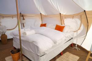 Posto letto in tenda con lenzuola bianche e cuscini arancioni. di Safari Desert Camp a Shāhiq