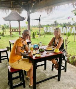 un hombre y una mujer sentados en una mesa con comida en Kubu Bakas Guest House - CHSE Certified, en Banjarangkan