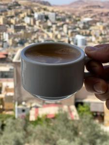 une personne tenant une tasse de café dans une ville dans l'établissement Petra Wooden House, à Wadi Musa