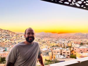 a man standing on a balcony with a view of a city at Petra Wooden House in Wadi Musa