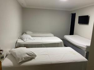 a room with three beds and a flat screen tv at Nasser Hotel Aeroporto in Núcleo Bandeirante