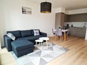 a living room with a blue couch and tables and a kitchen at Demims Apartments Lillestrøm - Modern & Super Central - 10mins from Oslo S in Lillestrøm