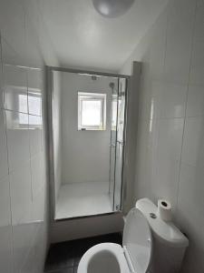 La salle de bains blanche est pourvue d'une douche et de toilettes. dans l'établissement Hatton Homes: Tottenham (Thackery Avenue), à Londres
