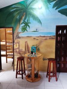 a table with two stools and a palm tree mural at Hostel Alto Astral - Fonte in Morro de São Paulo