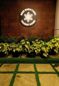 un panneau sur un bâtiment avec des plantes devant lui dans l'établissement SREENARAYANA TOURIST HOME, à Guruvāyūr