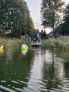 a child in a kayak on a lake with a dock at Okno Na Wodę- całoroczne domy z linią brzegową jeziora i sauną in Rybno