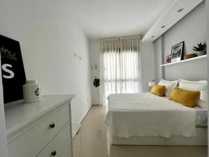 - une chambre blanche avec un lit et des oreillers jaunes dans l'établissement Apartamentos Gran Sol con jardin, à Ciudad Quesada