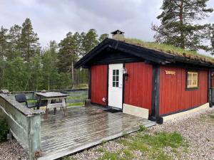 uma cabina vermelha com um telhado de relva e um deque de madeira em Atnasjø Kafe AS em Sollia