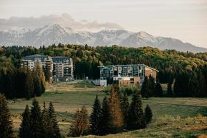 a building in a field with mountains in the background at Edelweiss Apartments SILVER RESORT POIANA BRASOV in Poiana Brasov