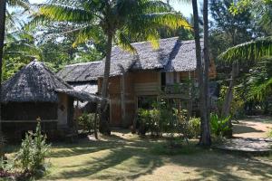 una casa antigua con techo de paja y palmeras en Bunga Jabe en Karimunjawa