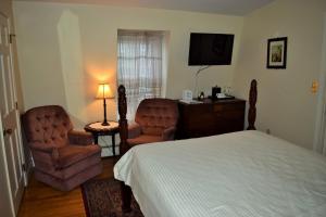 a bedroom with a bed and two chairs and a television at Inn on Bellevue in Newport