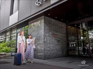 Daiwa Roynet Hotel Kyoto Shijo Karasuma في كيوتو: امرأتين واقفتين أمام مبنى مع حقيبة