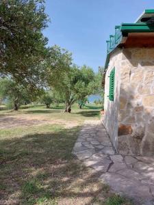a stone building with a green window next to a field at Robinson house Sea & olives in Tisno