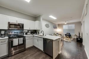 a kitchen with white cabinets and appliances and a living room at Modern 1BR Apt I Dallas City Center I Pool I Gym I Workspace I Pets in Dallas