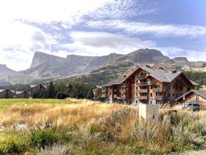 a building in a field with mountains in the background at APPARTEMENT CHALETS DU SUPER D in Le Dévoluy
