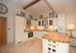 a large kitchen with white cabinets and a clock on the wall at The Cottage, Orgreave Estate in Yoxall