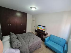 um quarto com uma cama e uma cadeira azul e uma televisão em Acogedor Departamento centrico em Cochabamba