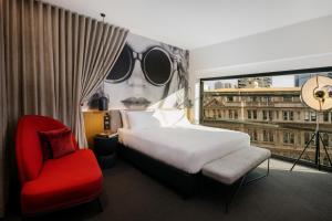 Hotel Indigo Melbourne on Flinders, an IHG Hotel في ملبورن: غرفة نوم بسرير وكرسي احمر ونافذة