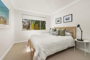 a white bedroom with a bed and a window at On Cyrus at Hyams Beach in Hyams Beach